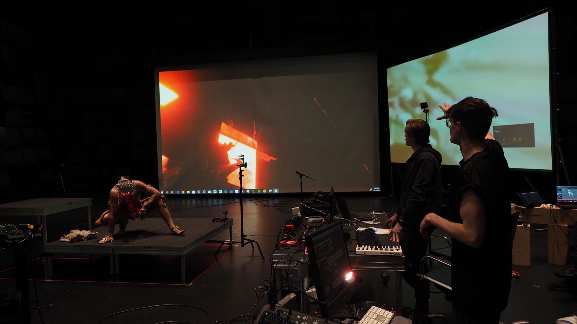 Justin Shoulder working with a dancer with multiple sensors attached to them in front of two large projection screens in black box studio.
