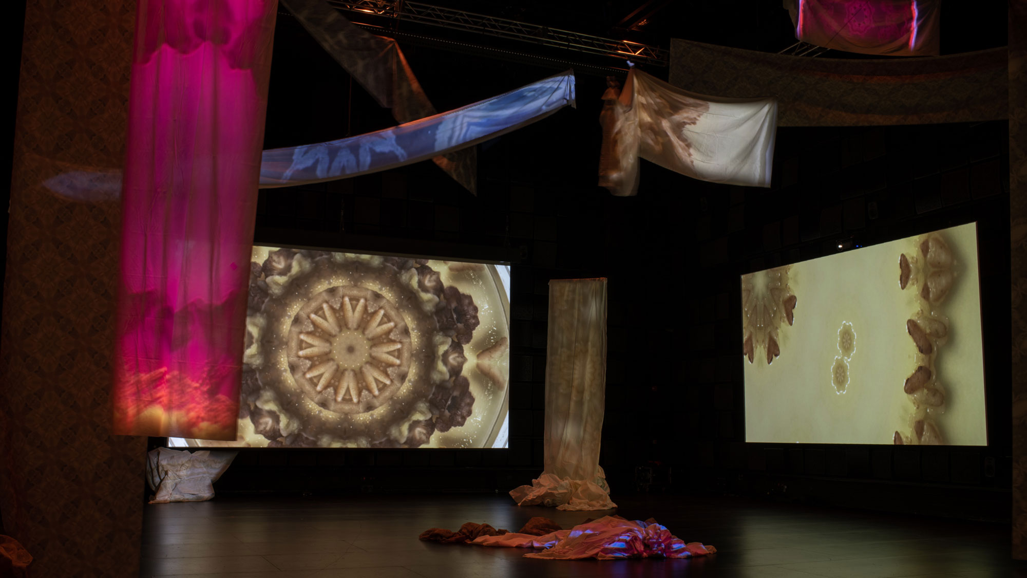 a room with tyedye colorful fabric hanging and geometric / biologic patterns projected on the fabric