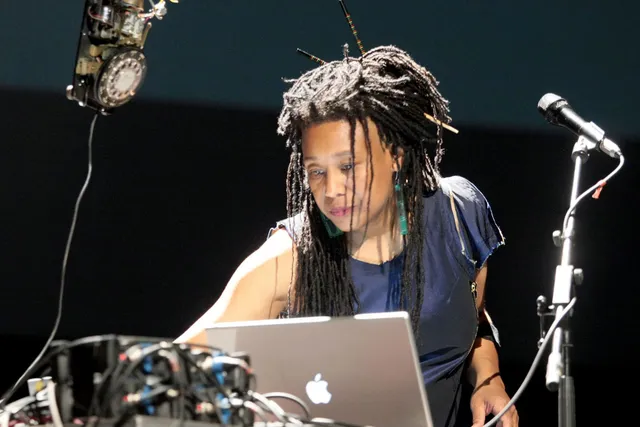 PamelaZ reaching across a lap top next to a microphone focused on the task in front of her. 