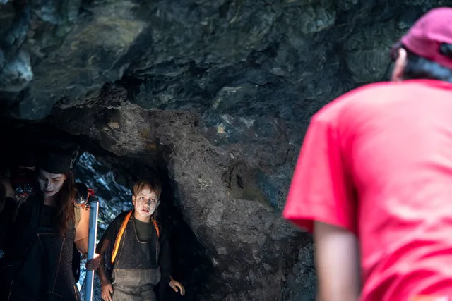 a camera person in the foreground directs a young child and adult in a cave 