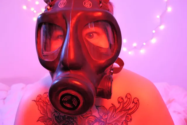 a shirtless tattooed person in a gas mask