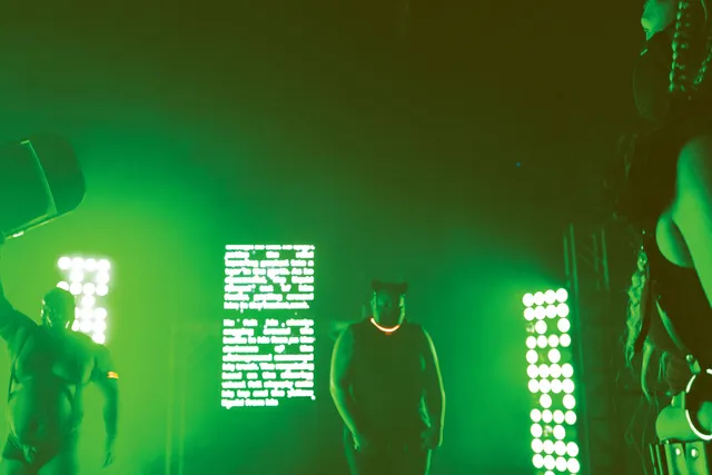 a group of black persons in bondage gear standing in a room lit with grass green light