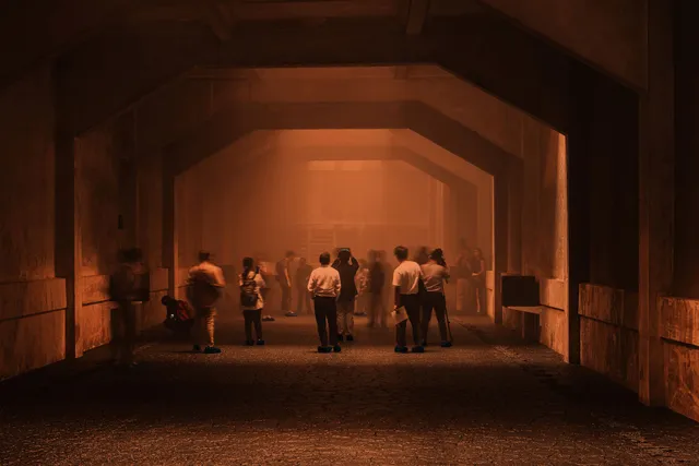 a group of people milling around at the end of an underground industrial structure with a sepia glow