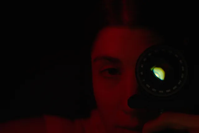 a woman in a dark red cast holds a strange device up to her left eye