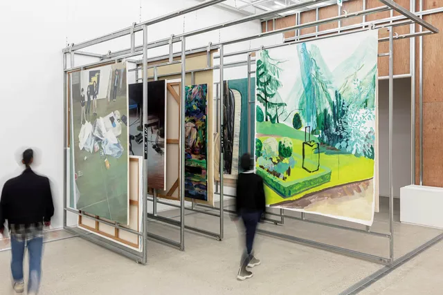 A large metal architecture inside a white-walled gallery hangs successive paints and drawings.