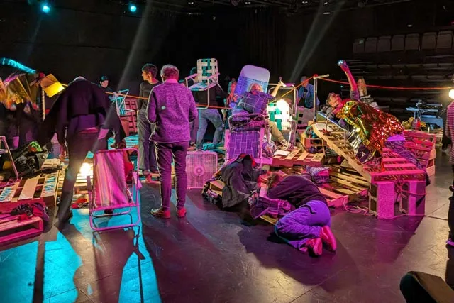 various people circling a pile of pallets and and other various objects in a black box studio