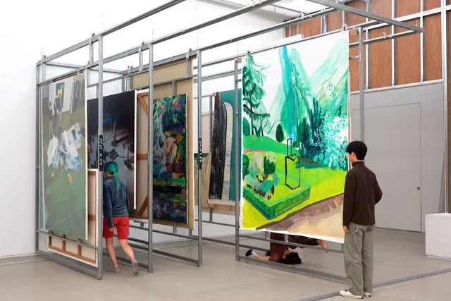 People weave in and out of large paintings mounted on parallel tracks within a metal art installation.