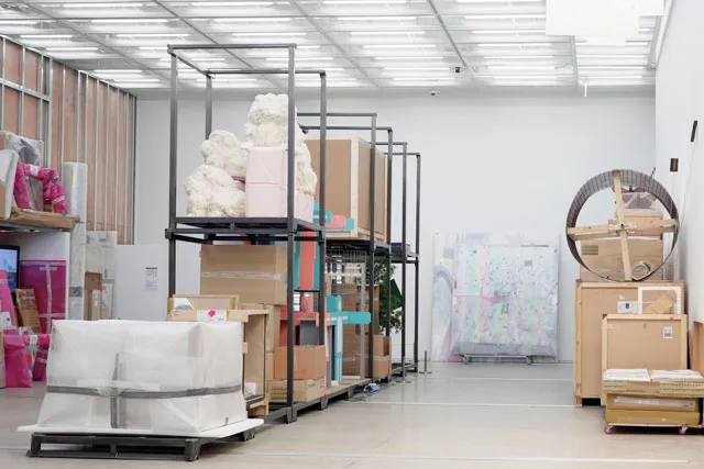 Large sculptures and packed boxes line the floors of a large gallery space. 
