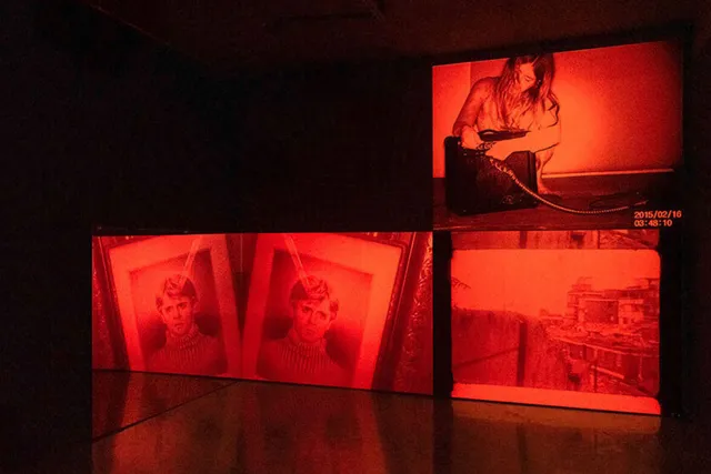 Three deep red images fill three screens, their light reflecting onto the floor.