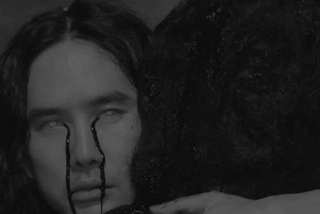 An asian person with long wavy hair crys black liquid while embracing another person with black liquid running throught their long black hair. 