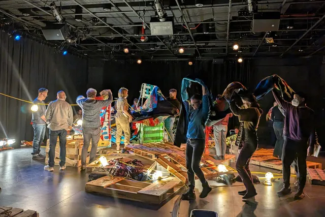 a group of people in a black box studio working around a structure made of wood shipping palettes