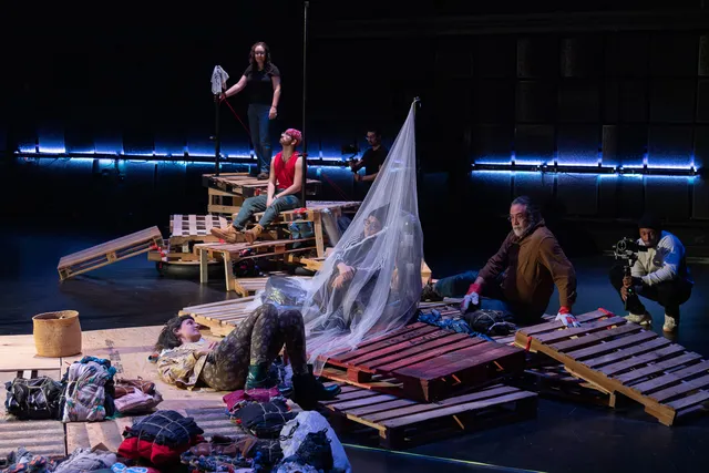a pile of wood pallets, clothing, and people in a black box studio