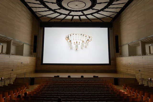 a still of a step-like dance team film on a massive screen in a concert hall