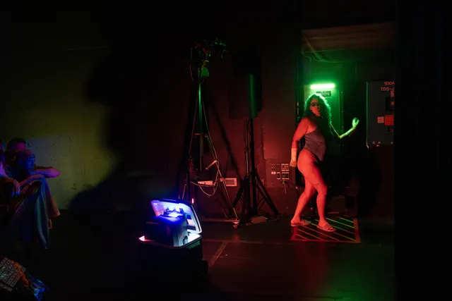a woman in a dark theater standing as if running next to a green fluorescent lamp