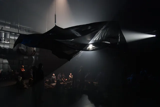 an ominous black canvas of fabric undulates above an audience in a black box studio