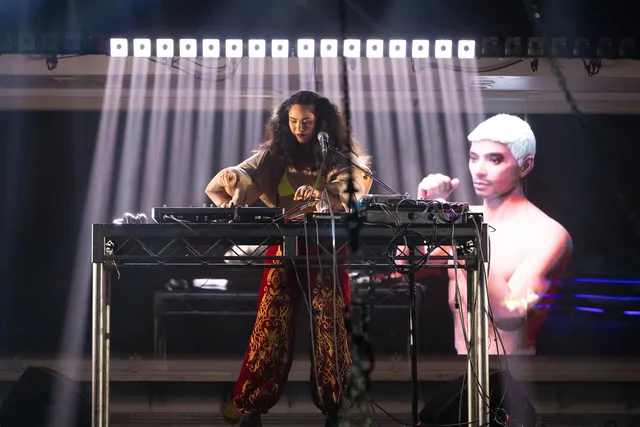 a woman at a keyboard with an image projection of a shirtless man in the background