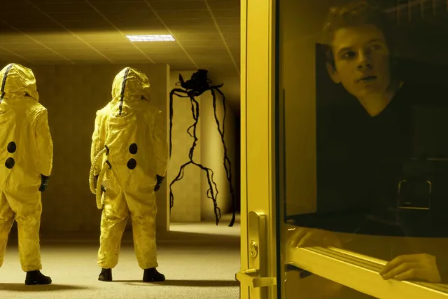 two people in space suits looking down the hall at a spider-like creature