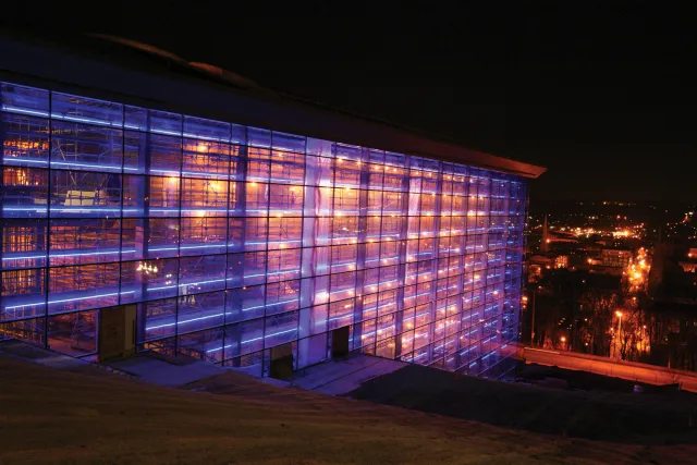 The nighttime exterior of EMPAC during its construction lit from within with blue and yellow light. 
