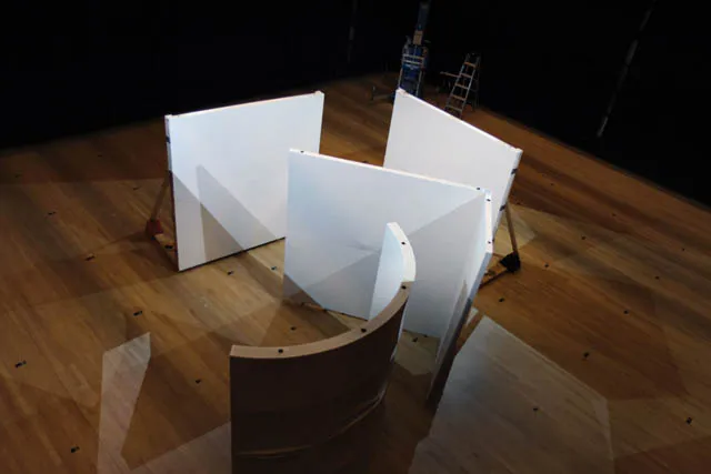 Four white set walls set up in a non sensical arrangement on a wooden stage. 