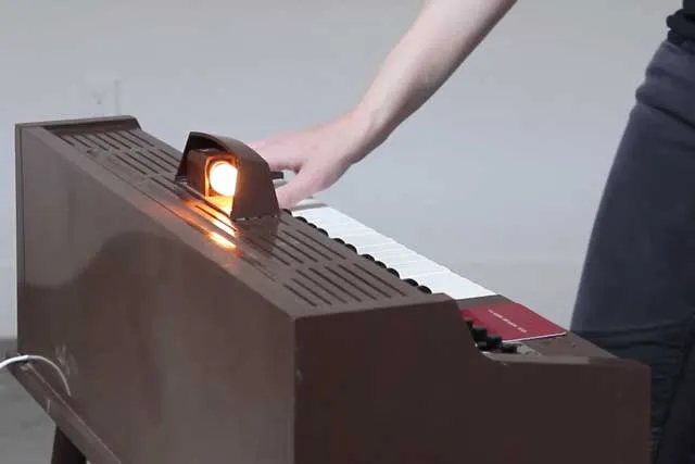 An adult hand playing a  brown toy piano. 