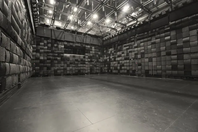 An empty black box studio with walls line with black acoustic tiles. 