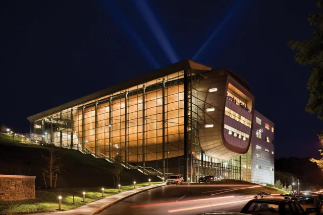  A night view of the side profile of EMPAC with beams of light behind the building. 