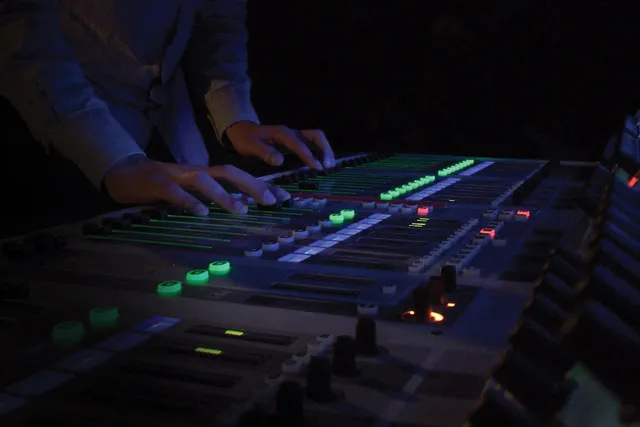 Hands on a sound board in a room that is lit only by the green buttons of the board. 