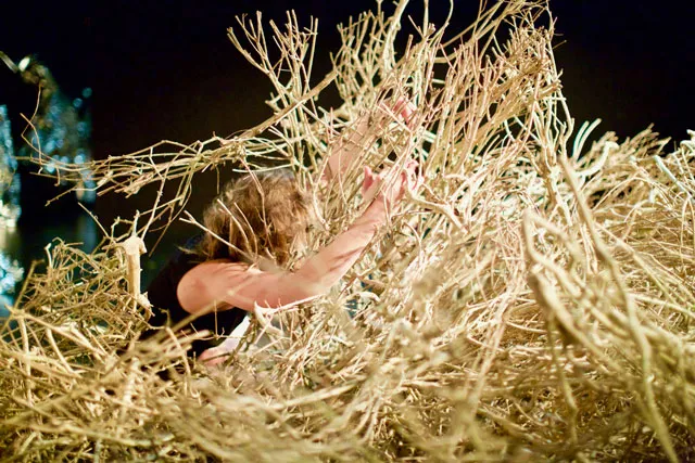 A person laying in a pile or nest of tan dried brush. 