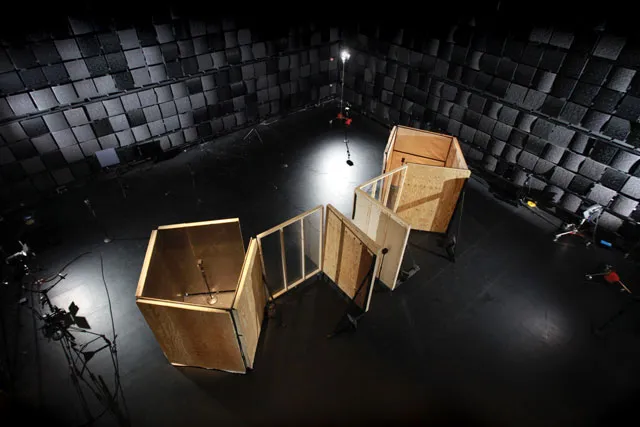An aerial view of two square wooden structures in an empty black box studio. 