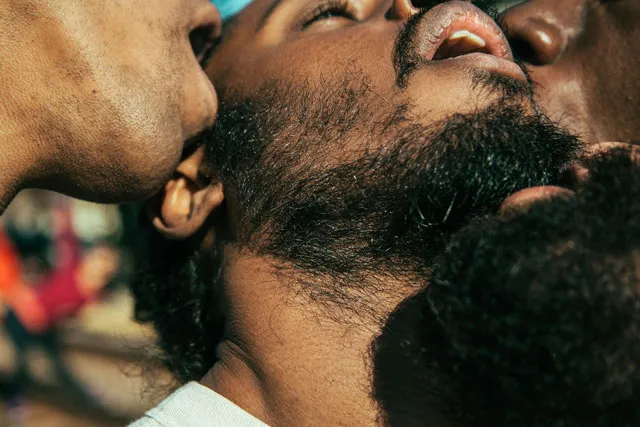 A tight shot of four Black men in close proximity with mouths open, sexual.