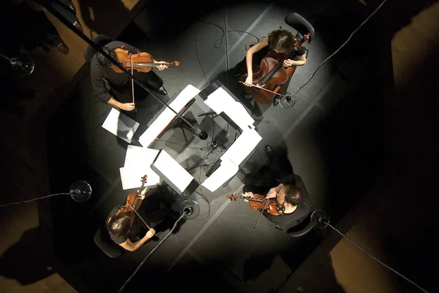 Above shot of a string quartet sitting with white sheet music on music stands in a square. 