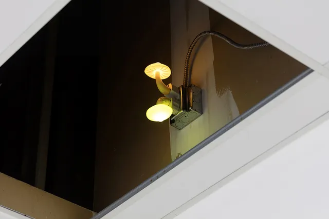 a mushroom shaped light plugged into a wall through a ceiling tile
