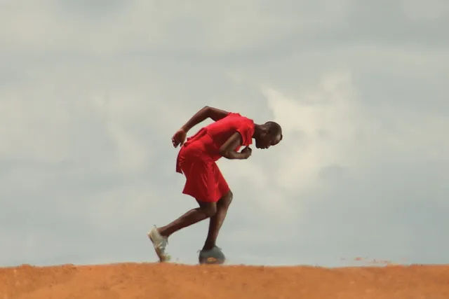 A Black person wearing red hunched in motion in a desert scene. 