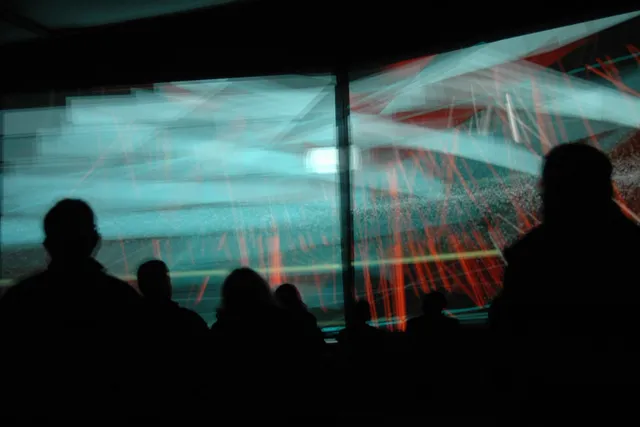 Teal and red abstract shapes projected on dual screens as a silhouetted audience looks on. 