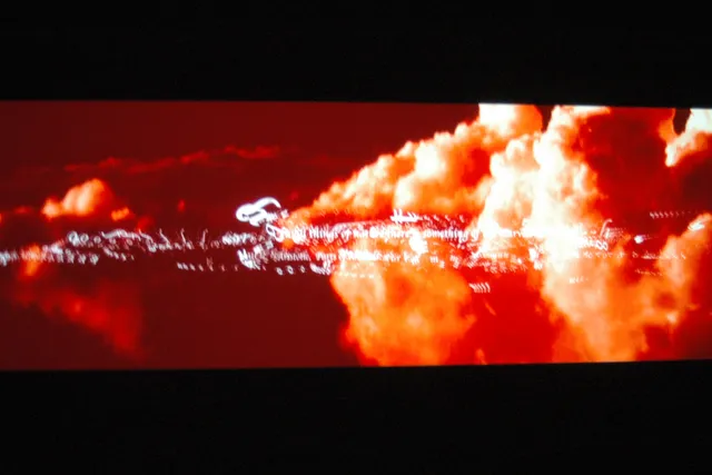 Red tinged clouds with illegible words in white script font across them projected on screen.