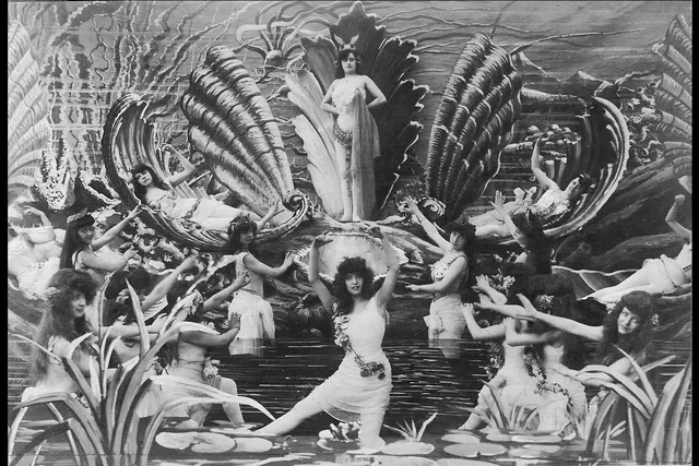 Film still of victorian woman dressed as water nymphs in a multi tiered ornate water scene. 
