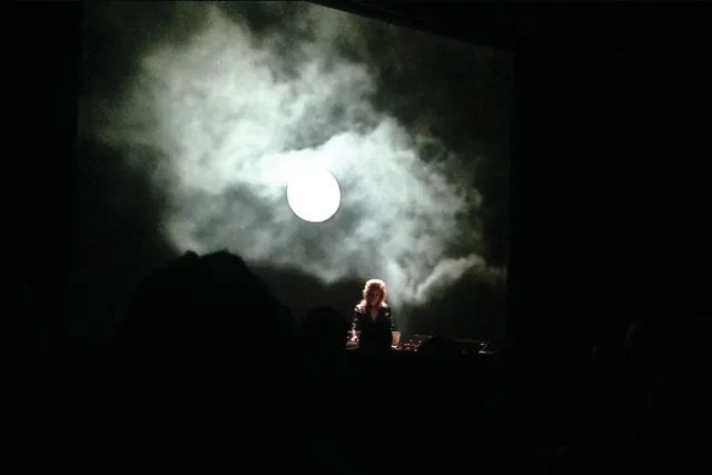 A person standing in a dark room in front of a projection of a cloudy night sky with a full moon
