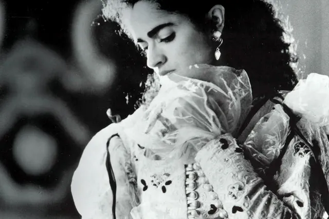 A woman wearing an ornate white dress with puffy sleeves and organza flares coming out of the bottom of the sleeve looking down over her shoulder dramatically. 