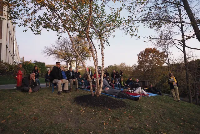A group of people seated on blankets and lawn chairs on the side of the empac hill in the fall. 