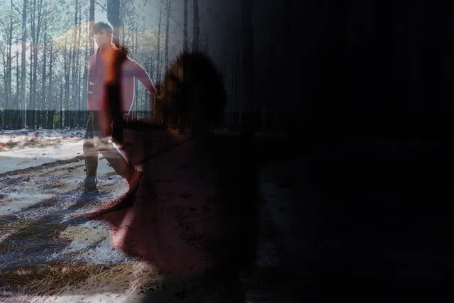 A double exposed image of a shadow of a woman reaching and a man wearing a red jacket walking through a sun dappled forest. 