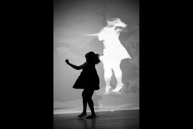 An inverse shadow of a young Black girl twirling with arms outstretched in a dress. 