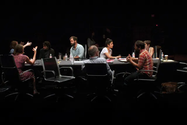 A group of eight in active discussion sitting around a conference table in a darkened room. 