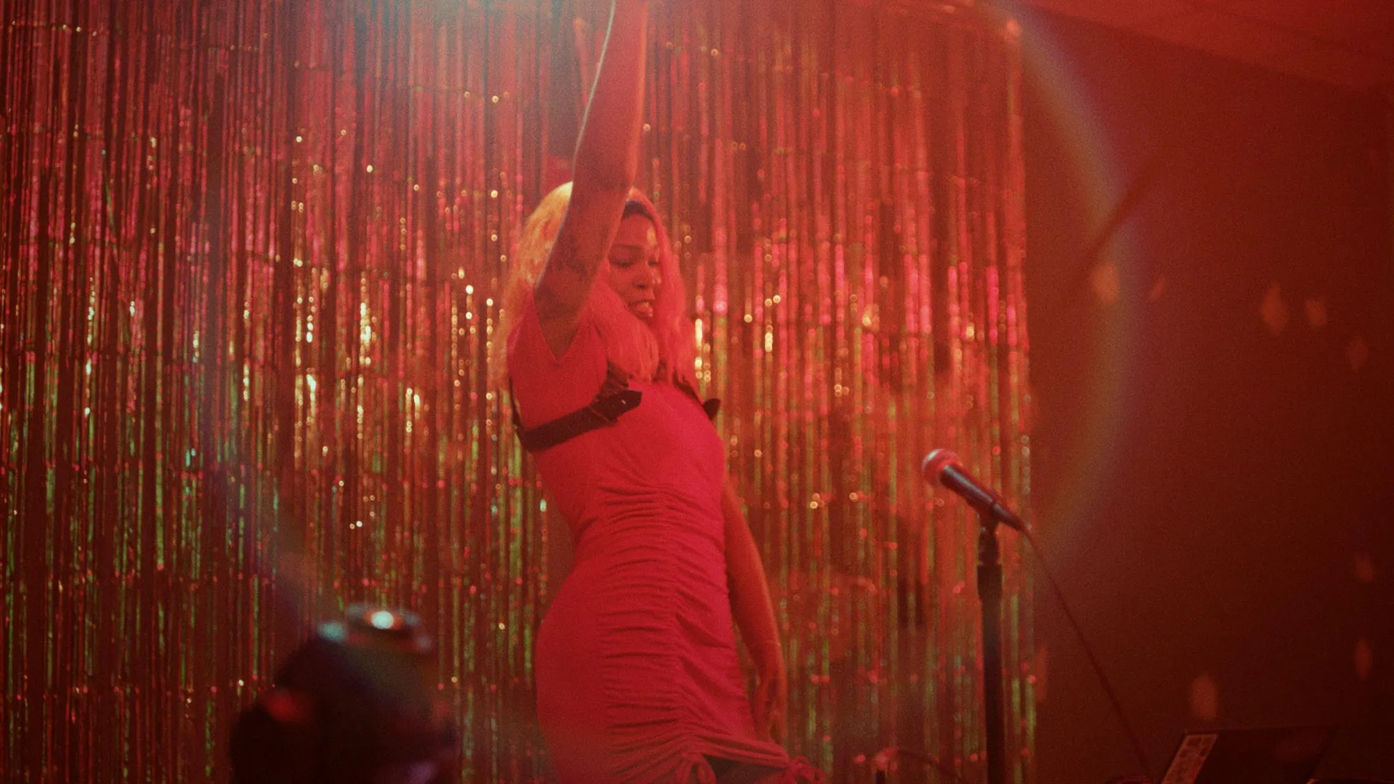 a black woman on stage in a red dress holds up her arm.