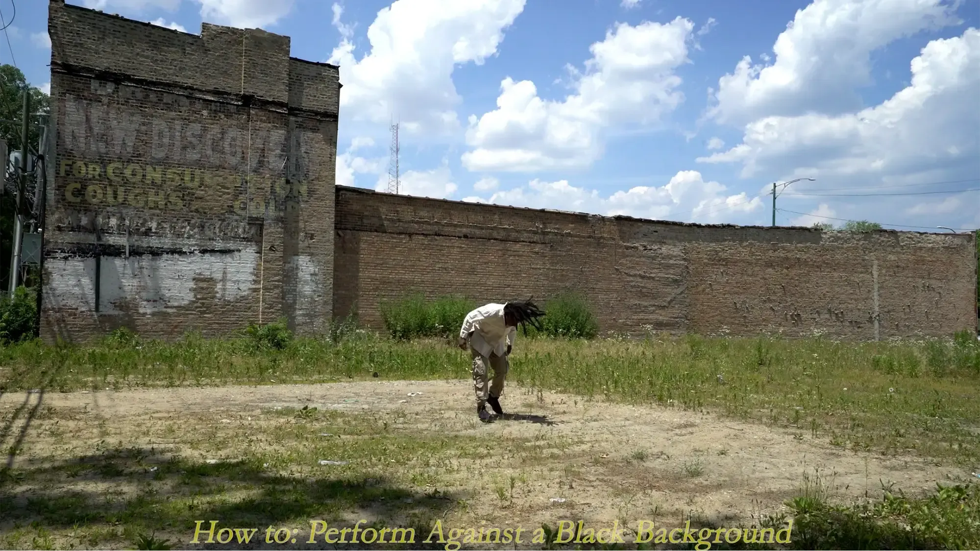 a person crouched in a field behind a old brick building