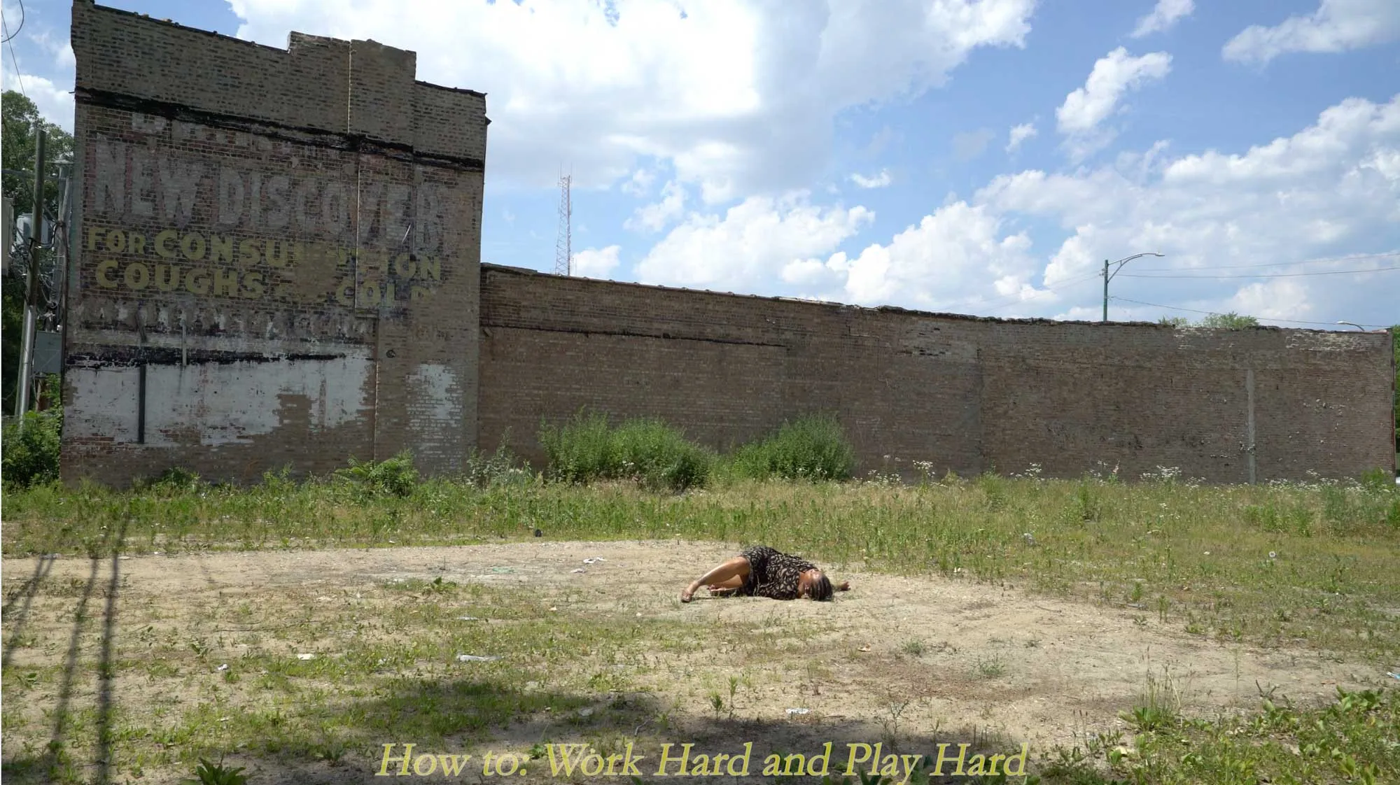 a Black woman laying in a field surrounded by an old brick building