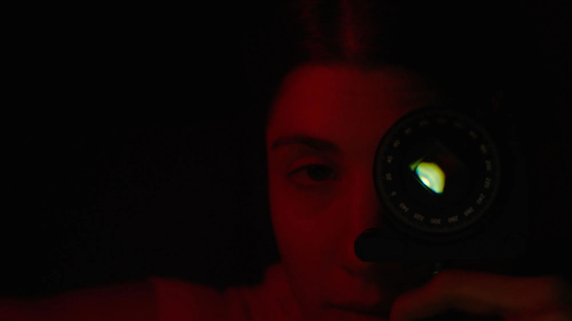 a woman in a dark red cast holds a strange device up to her left eye