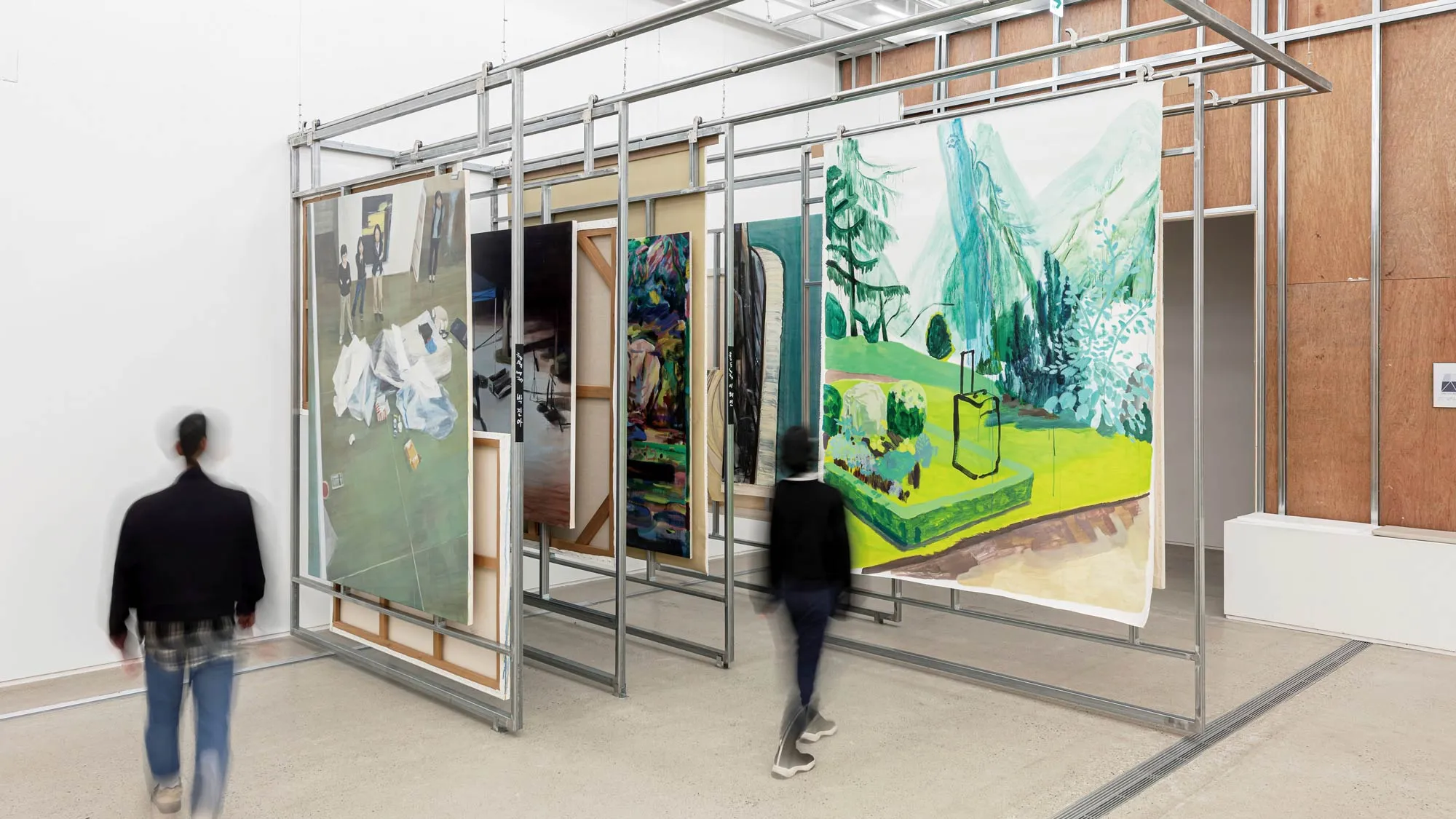 A large metal architecture inside a white-walled gallery hangs successive paints and drawings.