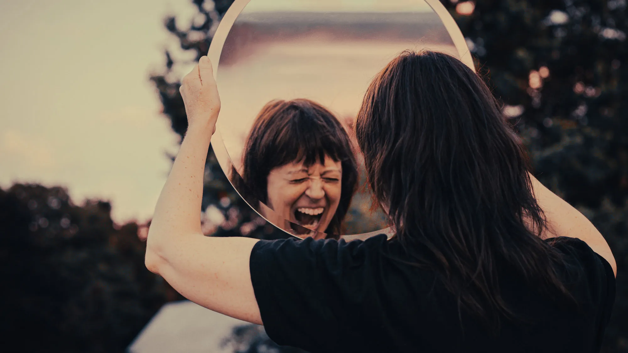 a woman holding a round mirror screaming with her eyes closed
