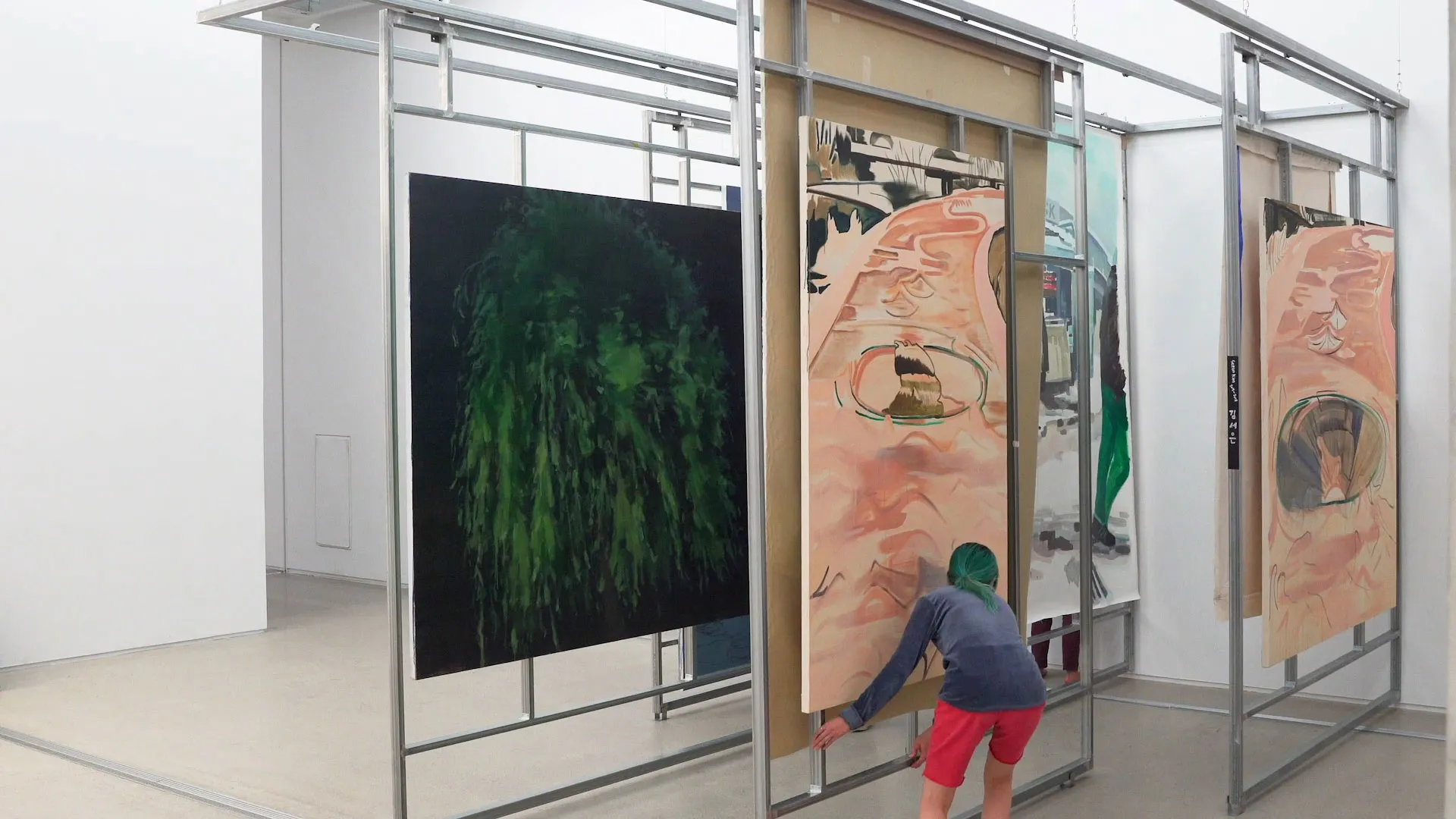 People weave in and out of large paintings mounted on parallel tracks within a metal art installation.