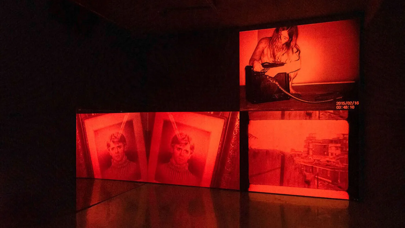 Three deep red images fill three screens, their light reflecting onto the floor.